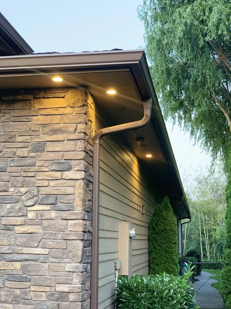 Dark brown aluminum gutters and downspout on a home with stone accents and soffit lighting