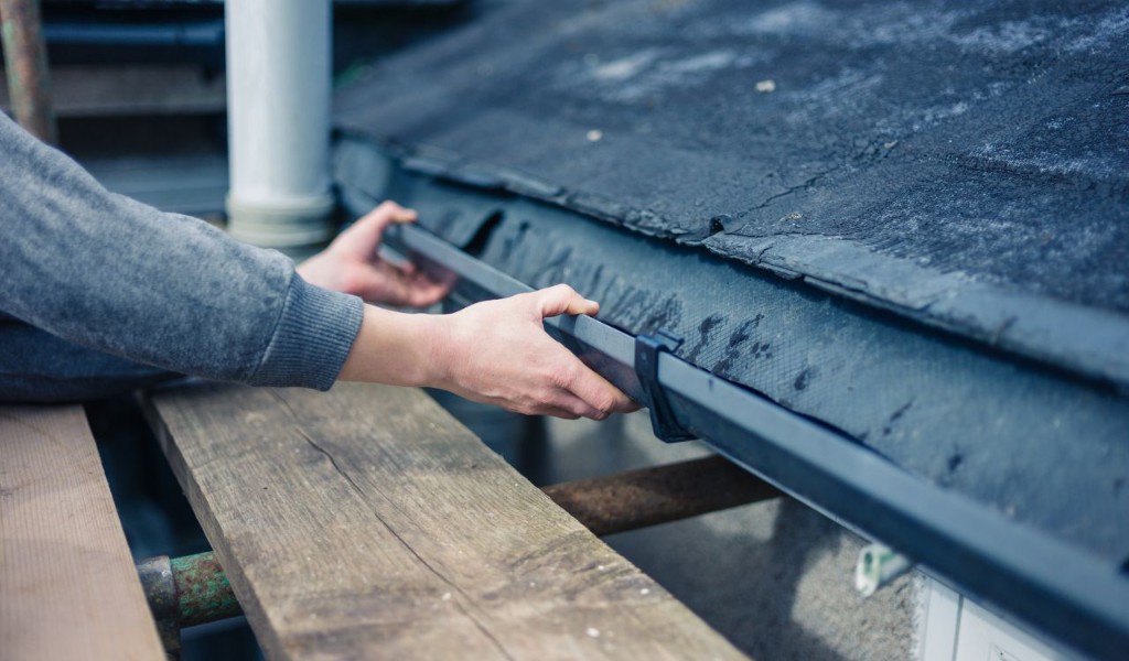 Technician installing a dark gutter section along a residential roofline from scaffolding